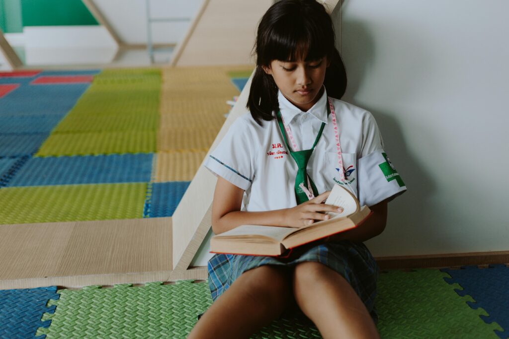 A student in a school uniform reading while sitting on the colorful classroom floor.