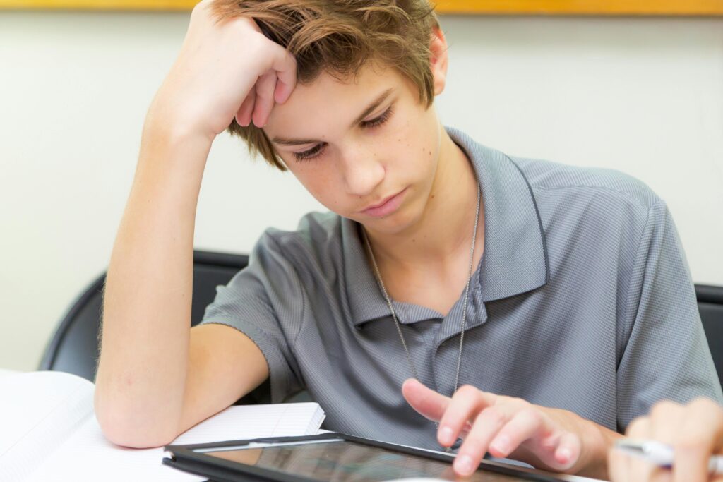 Focused teenager using a tablet for studying in a classroom environment.